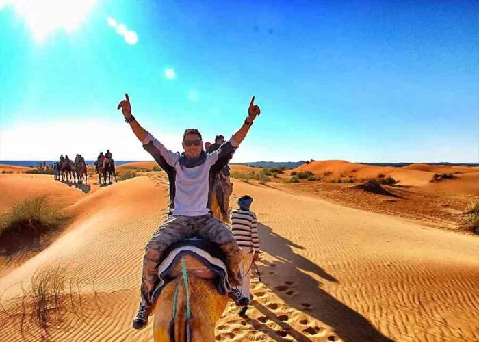 Tourist enjoying a camel ride in the Moroccan desert with others following on a clear day.