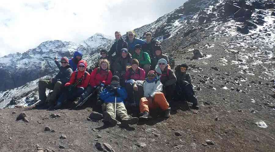 Happy trekkers resting on a 4-Day Mount Toubkal Trek with snowy peaks in the background.