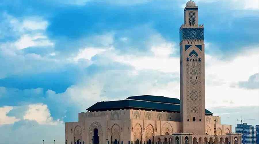 The Hassan II Mosque, a key destination on Marrakech to Casablanca day trips, looms over the Atlantic Ocean with its impressive 210-meter minaret under a clear blue sky.