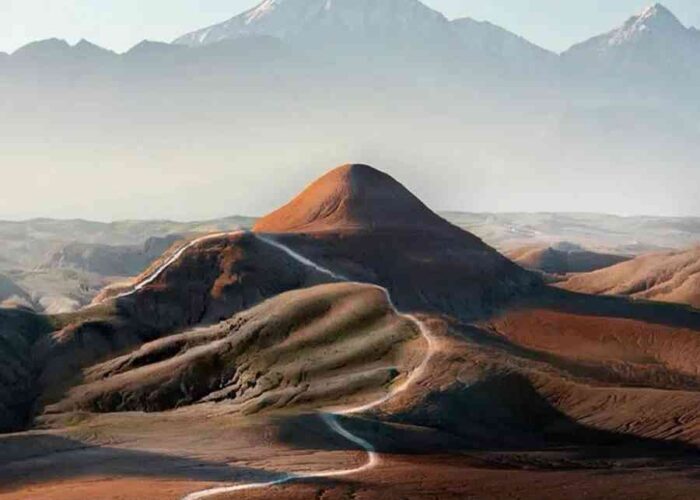 Scenic view of Agafay Desert with rolling dunes, a winding path, and distant mountains under a clear sky.