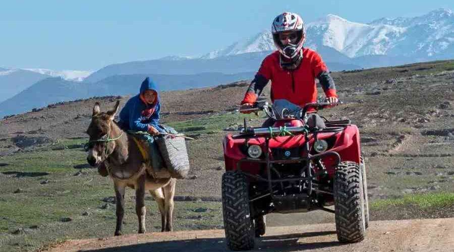 A quad biker and a local on a donkey on a trail with the Atlas Mountains in the distance.