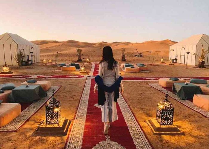 Woman walking towards luxury tents on a Marrakech to Fes desert tour at sunset