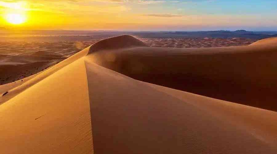 Sunrise over the Erg Chebbi dunes paints the sky with hues of orange and pink as the golden sands stretch out beneath, creating a breathtaking and serene desert vista.