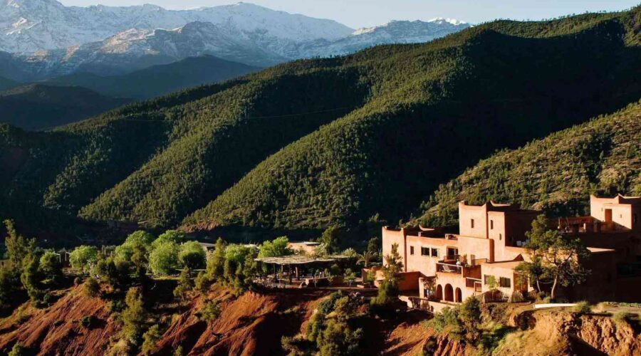 Luxurious mountainside retreat overlooking the verdant slopes of Ourika Valley with snow-capped Atlas Mountains in the distance.