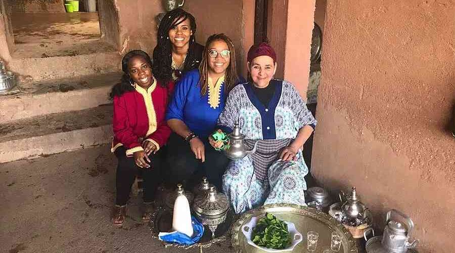 A group of tourists enjoying a cultural exchange with a local Moroccan woman during a day trip to the Atlas Mountains from Marrakech.