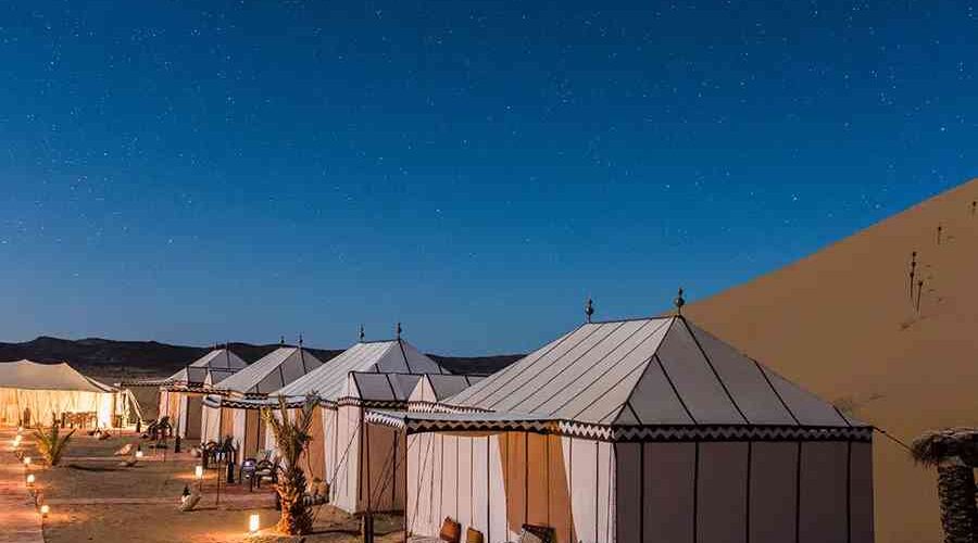 Luxurious desert camp tents under a starlit sky adjacent to Sahara dunes.