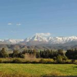 Scenic view of the snow-capped Atlas Mountains from Ourika Valley near Marrakech, with lush green fields in the foreground.