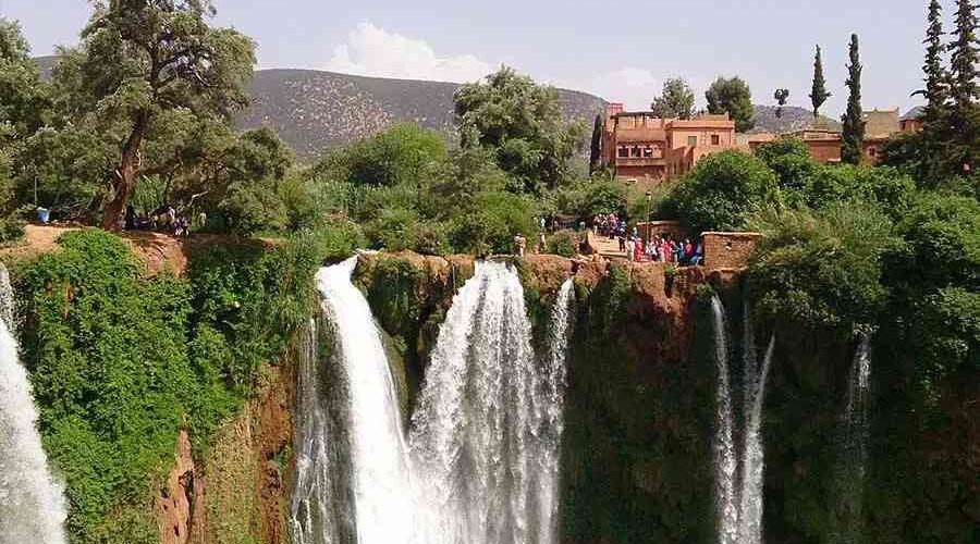 Visitors gather to admire the dramatic drop of the Ouzoud Waterfalls with traditional architecture in the background.