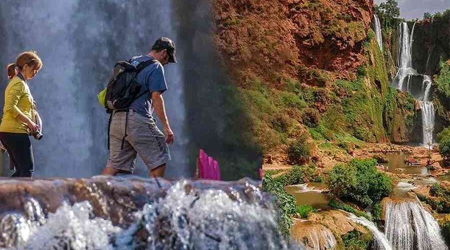 Two hikers exploring the Ouzoud Waterfalls with mist rising from the cascading waters and lush greenery in the background.