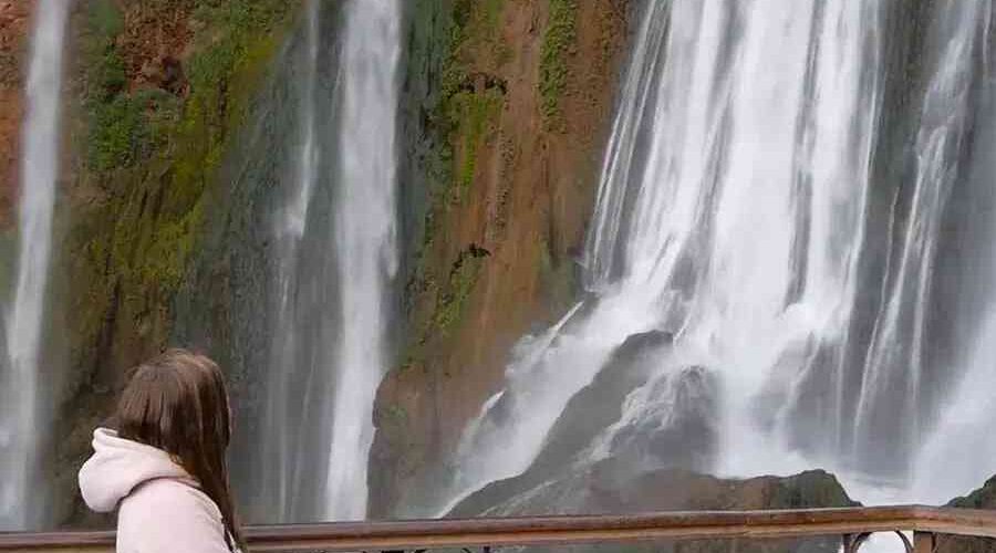 A visitor admiring the powerful flow of Ouzoud Waterfalls from a viewing platform.