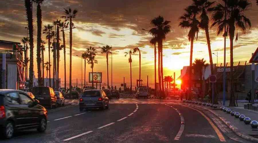 Sunset view along the Ain Diab Corniche in Casablanca, lined with palm trees and bustling with early evening traffic.