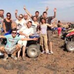 Group of happy tourists on a Marrakech adventure tour, with quad bikes and camels in the background, celebrating their desert experience.