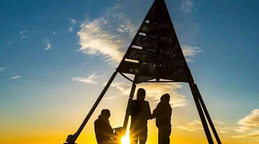 Silhouettes of hikers celebrating at dawn under the triangular summit marker of Mount Toubkal.