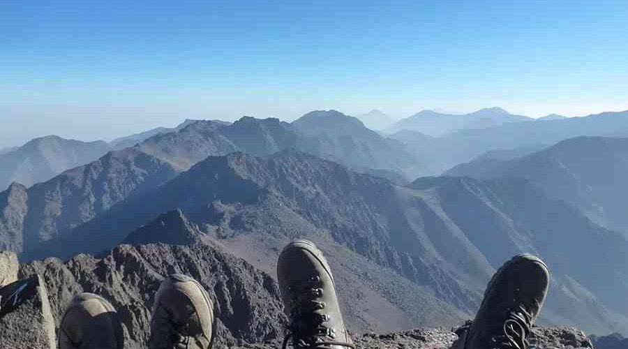 "Hikers' boots overlooking a panorama of layered mountain ridges from the summit of Mount Toubkal.