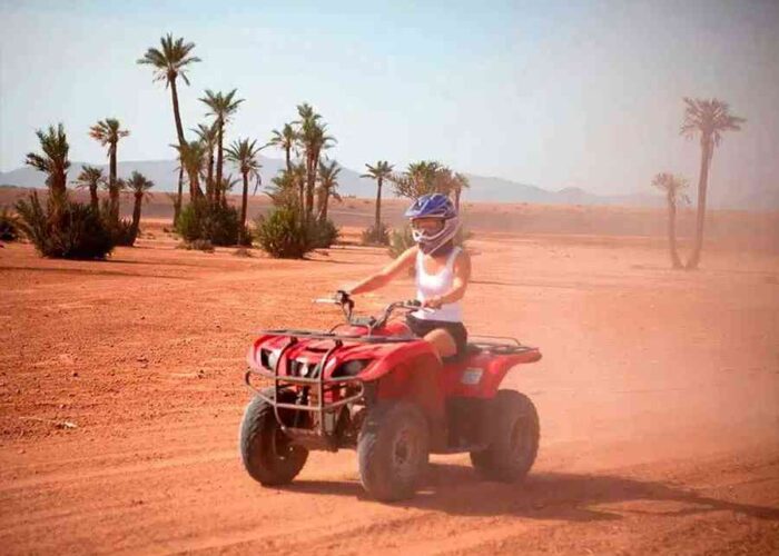 Adventurous tourist quad biking in the Marrakech desert with palm trees in the background.