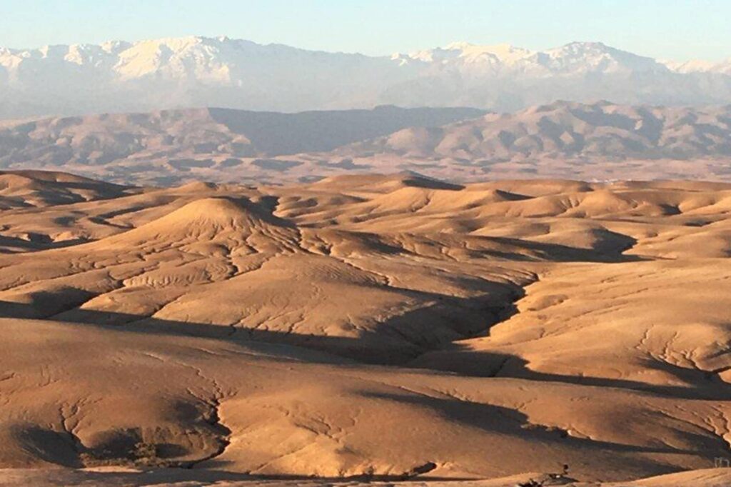 Golden hour over the undulating terrain of the Agafay Desert with the Atlas Mountains in the backdrop.