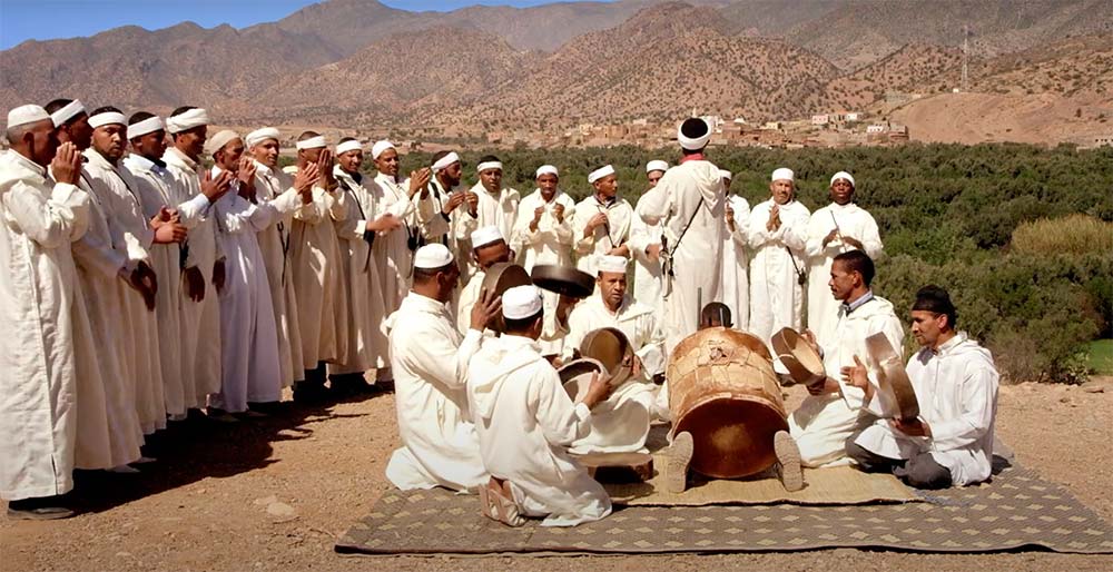 Group of Berber men in traditional white attire performing a musical ceremony with drums in the Atlas Mountains.