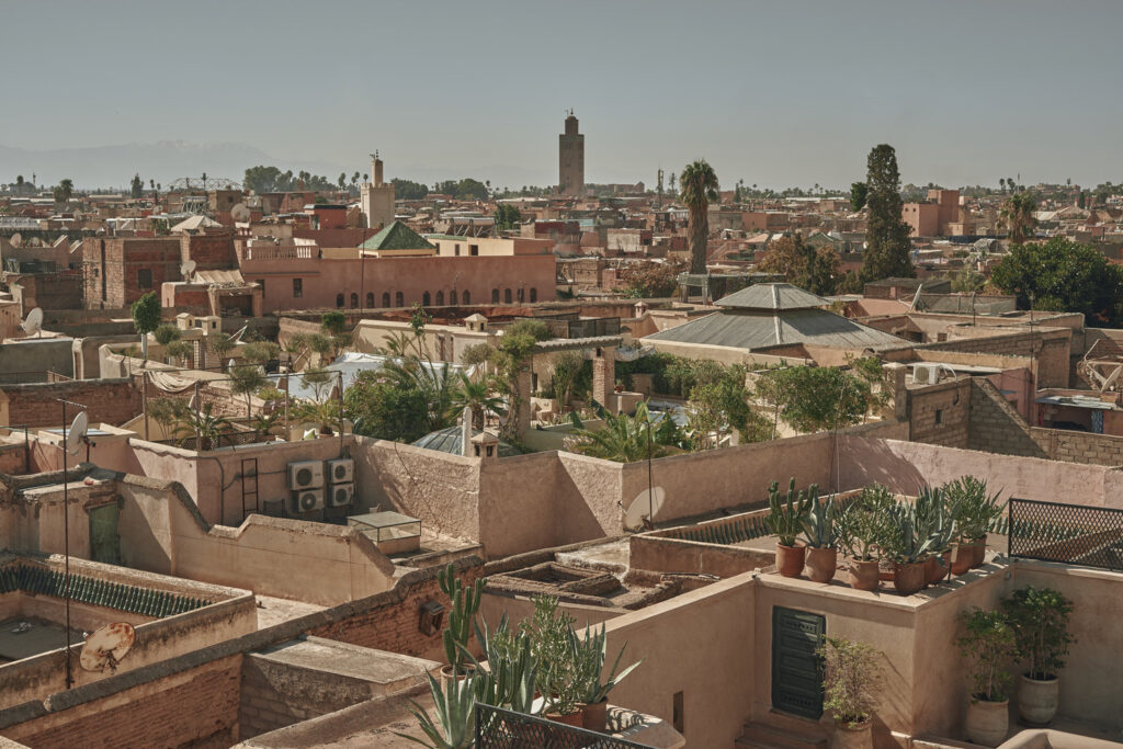 Panoramic view of the Bab Doukala neighborhood in Marrakech, with traditional terracotta rooftops and distant Atlas Mountains.