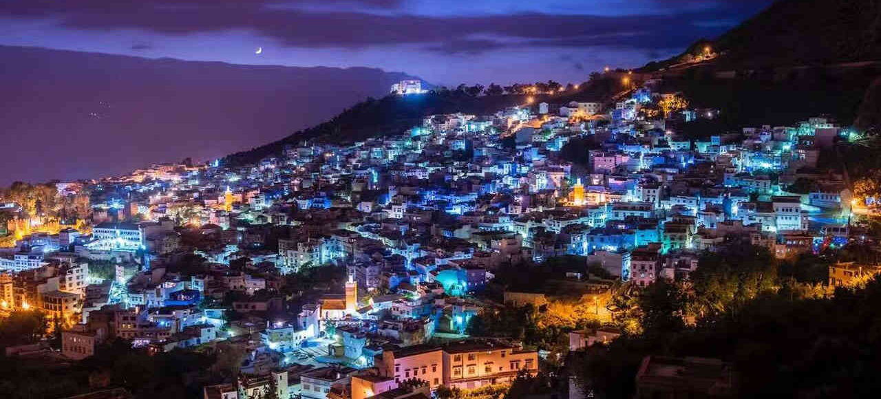 Night view of Chefchaouen, Morocco, with its iconic blue houses illuminated under a twilight sky.