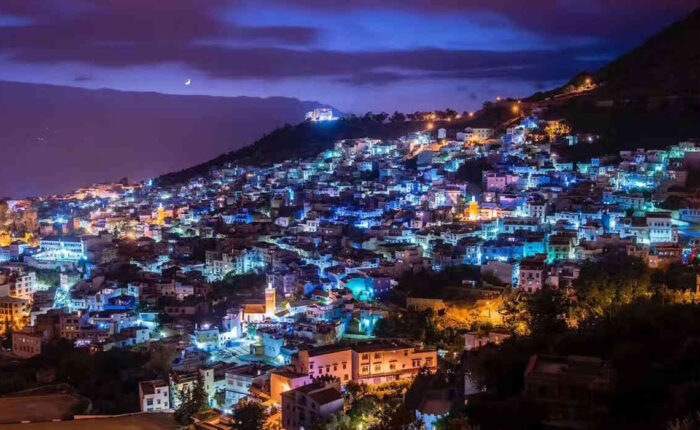 Night view of Chefchaouen, Morocco, with its iconic blue houses illuminated under a twilight sky.