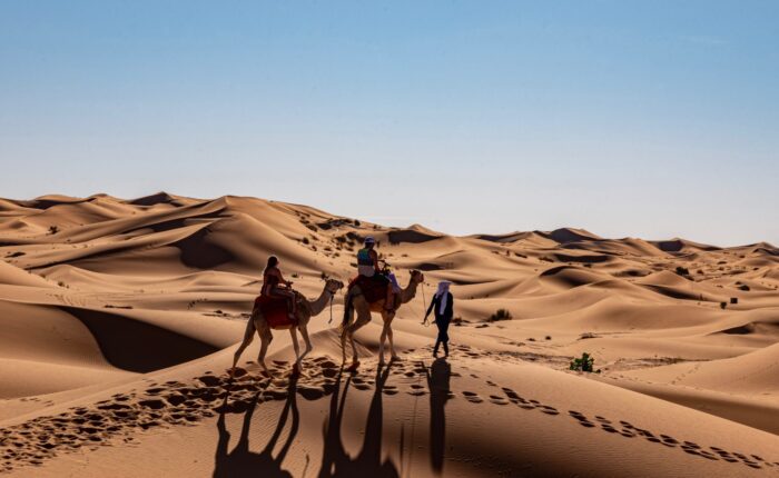 Couple riding camels in Erg Chigaga dunes, accompanied with a camel guide leading them to their Sahara desert camp
