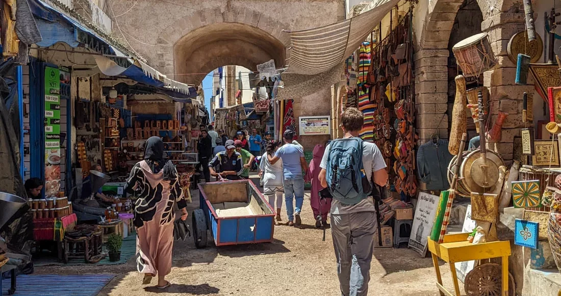 Tourists exploring the bustling souks of Essaouira with local shops displaying crafts and wares.