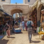 Tourists exploring the bustling souks of Essaouira with local shops displaying crafts and wares.