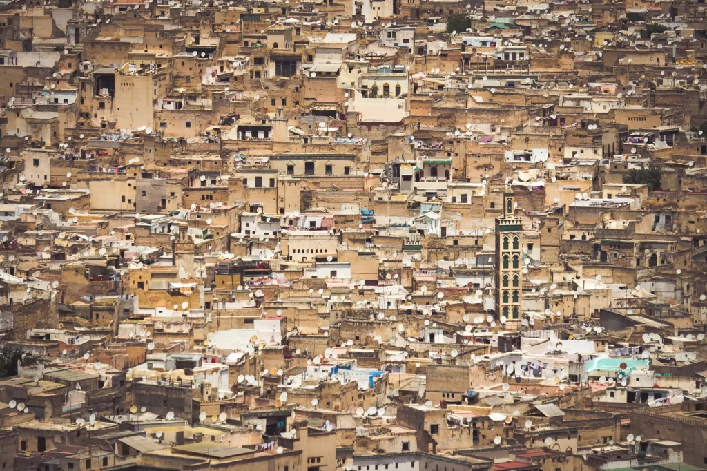 Dense aerial view of Fez Medina with traditional Moroccan architecture, crowded houses, and satellite dishes, under a hazy sky.