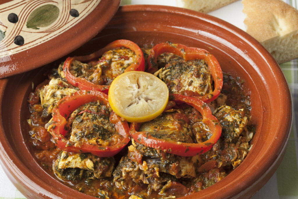 Traditional Moroccan fish tagine with tomatoes and lemon in a clay pot.