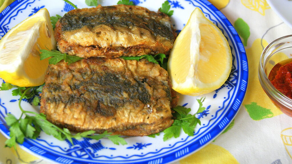 Fried Moroccan sardines on a decorative plate with lemon wedges and parsley.

