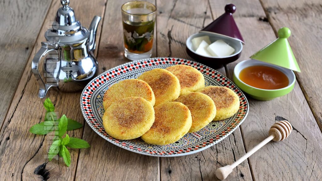 Golden-brown Harcha semolina pancakes on a decorative plate, served with Moroccan mint tea and honey.