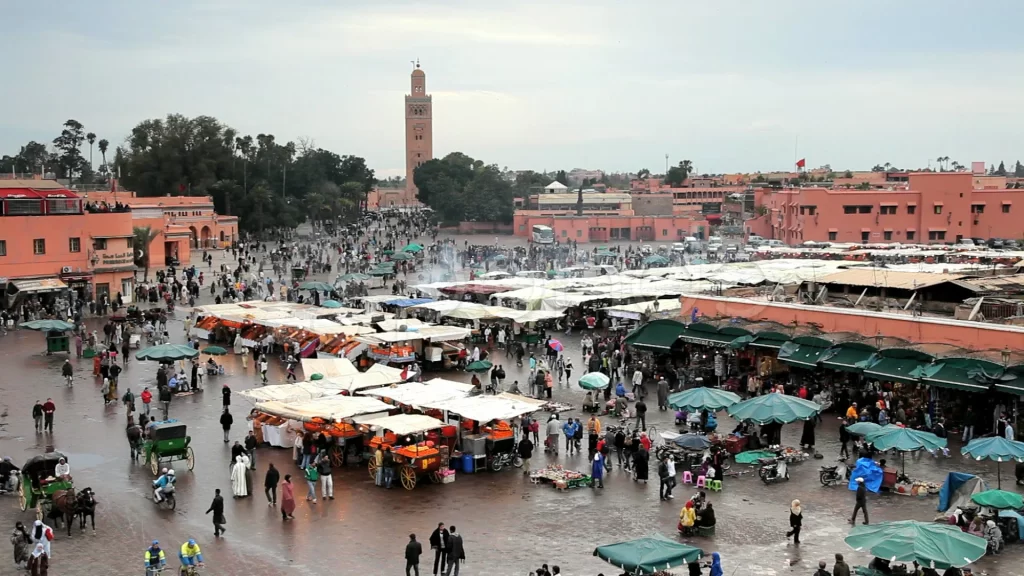 Dynamic Jemaa el-Fnaa square in Marrakech with crowds, market stalls, and the Koutoubia Mosque in the background.