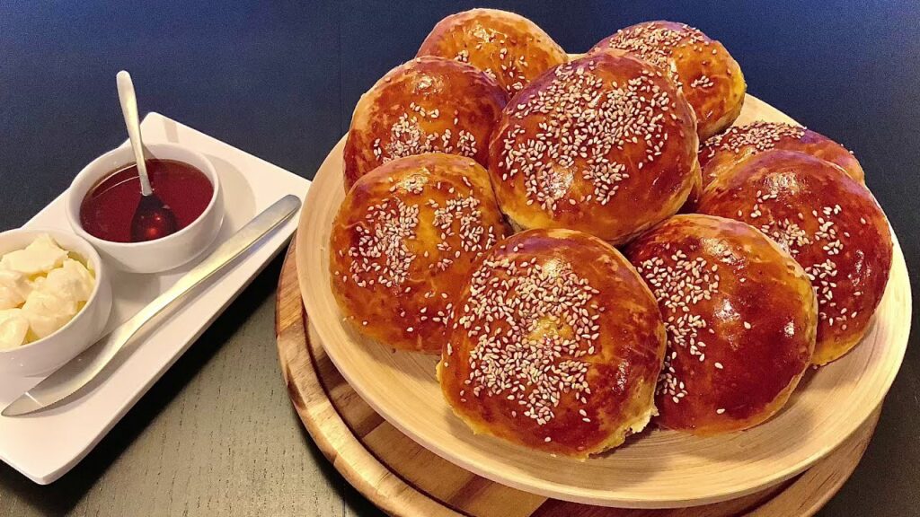 Glazed Moroccan Krachel buns sprinkled with sesame seeds on a wooden serving plate.
