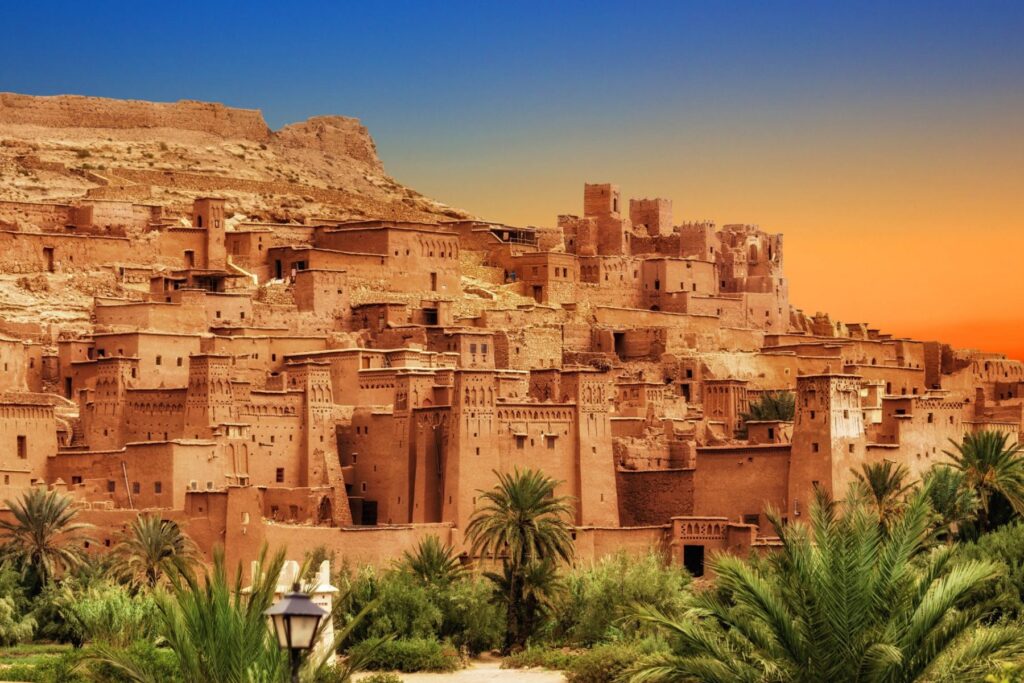 Sunset view of the ancient Kasbah Ait Ben Haddou in Morocco with palm trees.