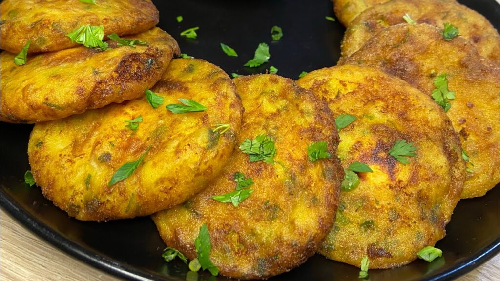 Golden-brown Maakouda patties garnished with fresh parsley on a black plate.