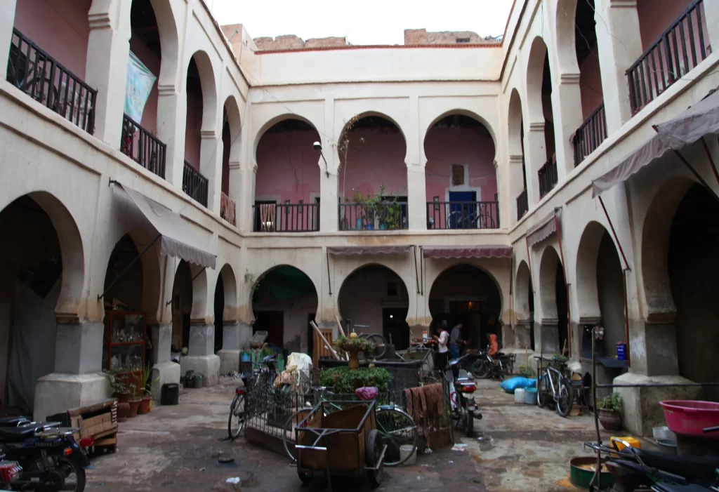 Inner courtyard of a historical foundouk in Marrakech, featuring arched galleries and everyday items scattered around.