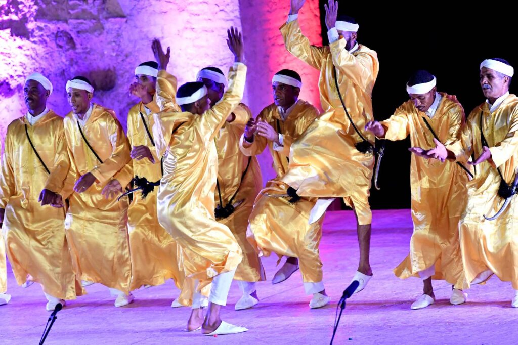 Group of musicians in golden attire performing a traditional dance at the Marrakech Popular Arts Festival.