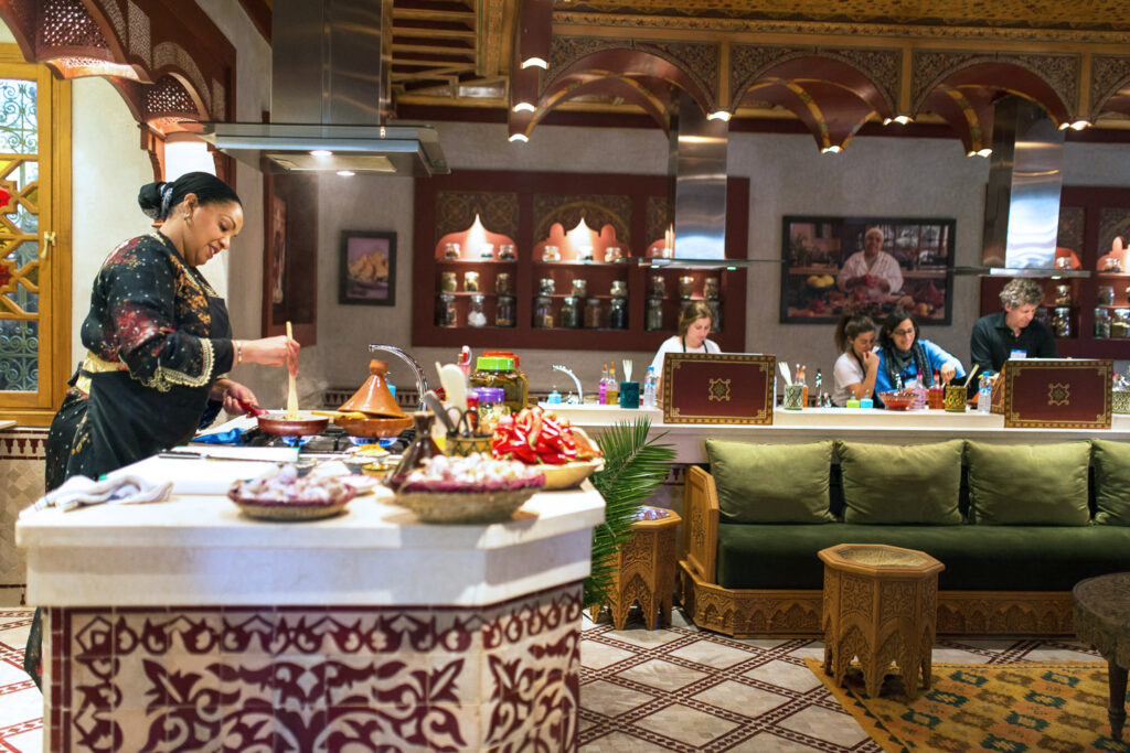 Chef preparing traditional Moroccan dishes during a cooking class in Marrakech with participants watching.