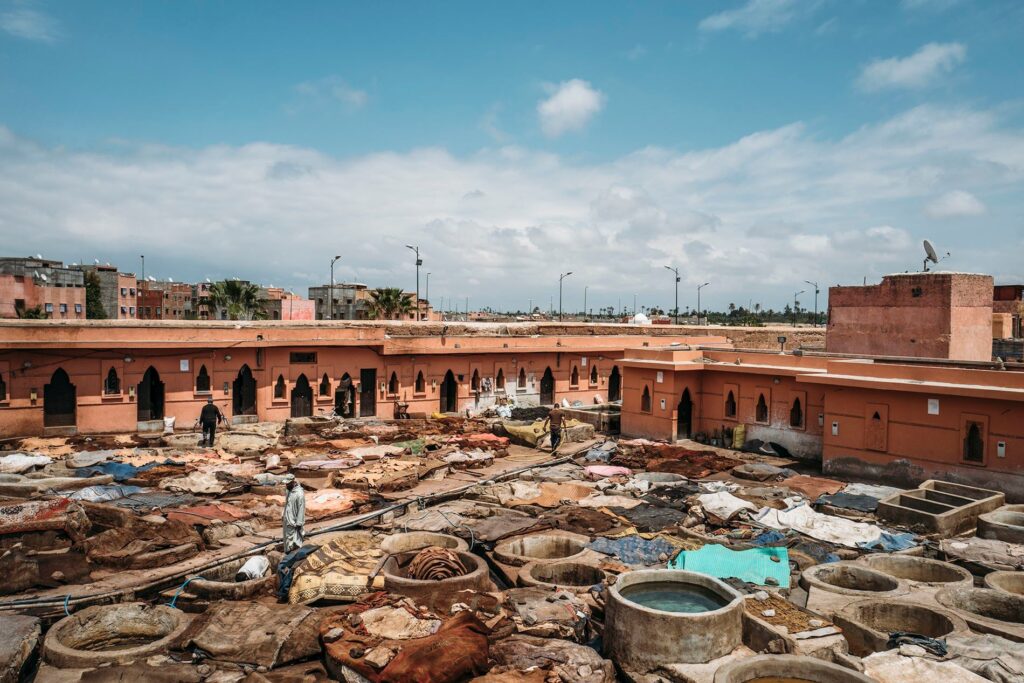 Active tannery in Marrakech with workers processing hides in stone vessels, surrounded by buildings.