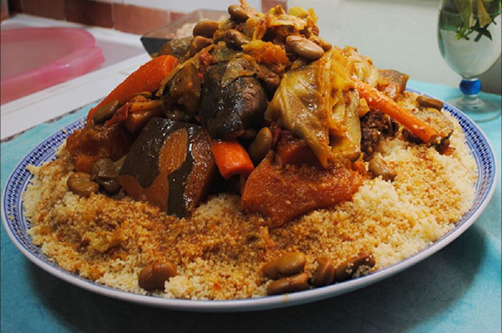 A traditional Moroccan Couscous dish served on a blue and white patterned plate, topped with a variety of steamed vegetables and legumes.