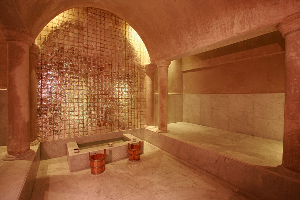 Elegant interior of a Moroccan hammam with warm lighting, marble benches, and traditional copper buckets.