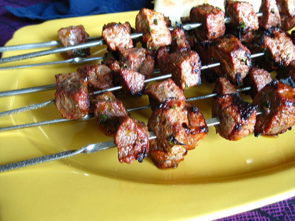 Grilled Moroccan lamb kebabs on skewers placed on a vibrant yellow plate.