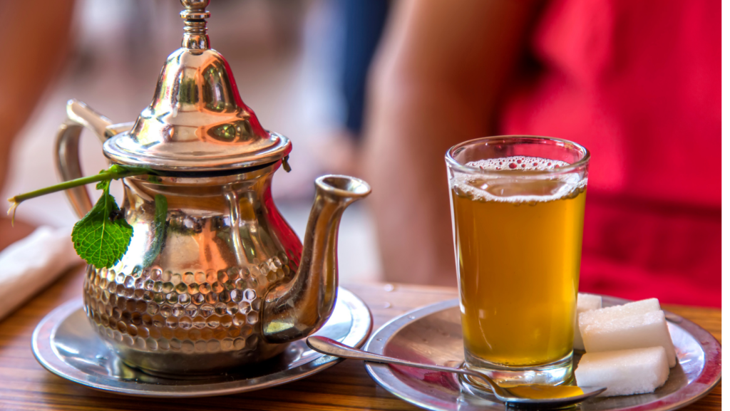 A traditional Moroccan mint tea set, with a silver teapot and a glass of tea garnished with fresh mint.