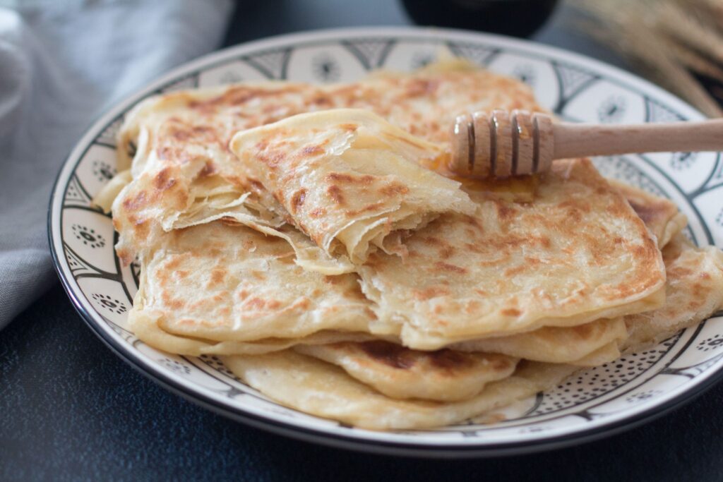 Moroccan Msemen flatbread drizzled with honey on an ornate plate.