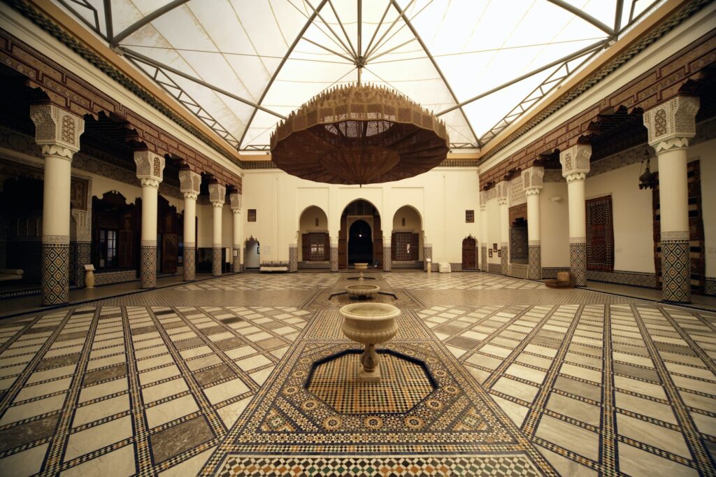Spacious courtyard of the Marrakech Museum with a traditional fountain, framed by ornate archways and mosaic tile flooring.