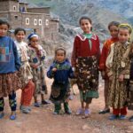 Berber kids posing for a photo at a Berber Village in the Atlas Mountains with mud brick humble houses in the back.