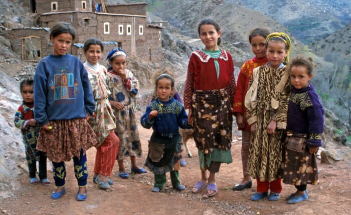 Berber kids posing for a photo at a Berber Village in the Atlas Mountains with mud brick humble houses in the back.