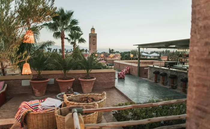 Cozy rooftop terrace of a Marrakech restaurant with views of Koutoubia Mosque amid palm trees at dusk.