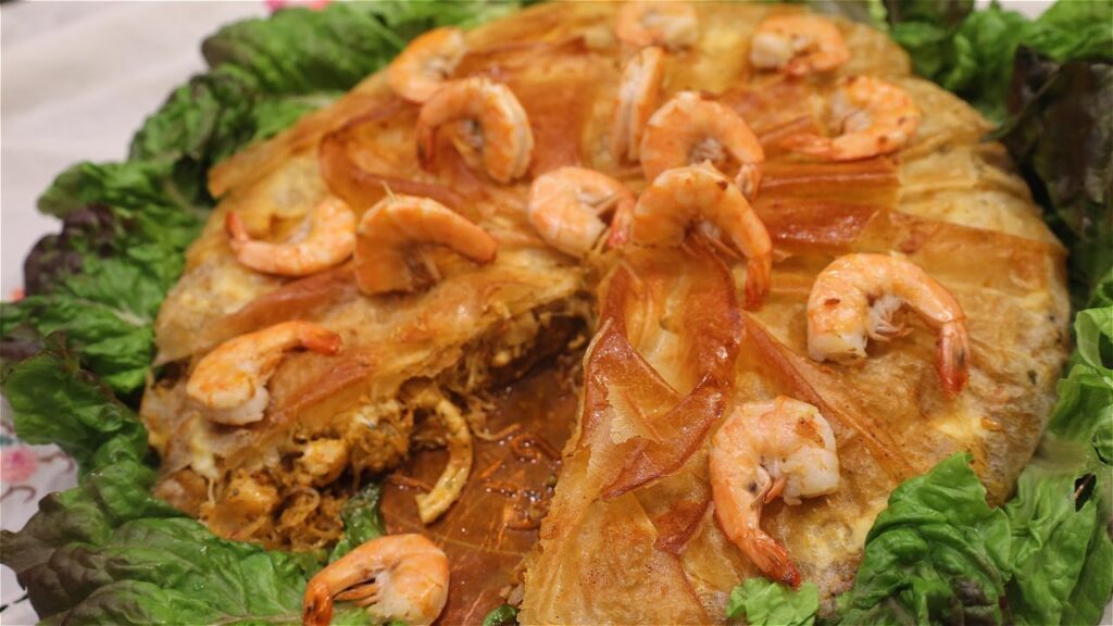 Seafood Pastilla topped with caramelized onions and shrimp on a bed of lettuce.
