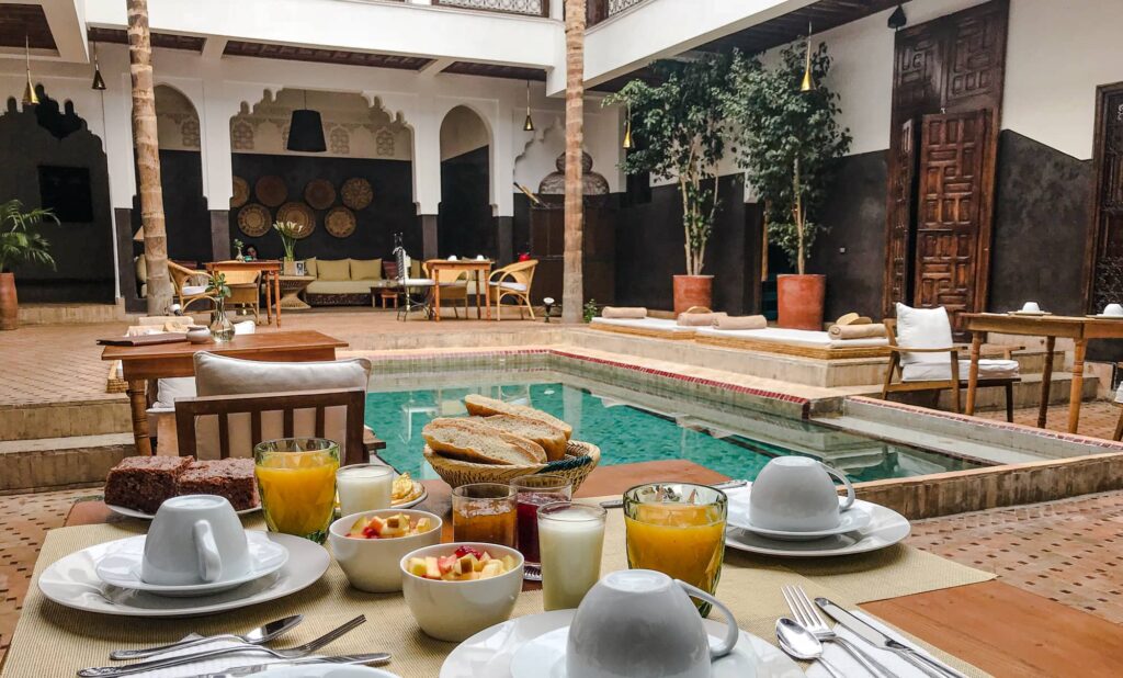 Luxurious breakfast spread by the tranquil pool inside a traditional Marrakech riad courtyard.